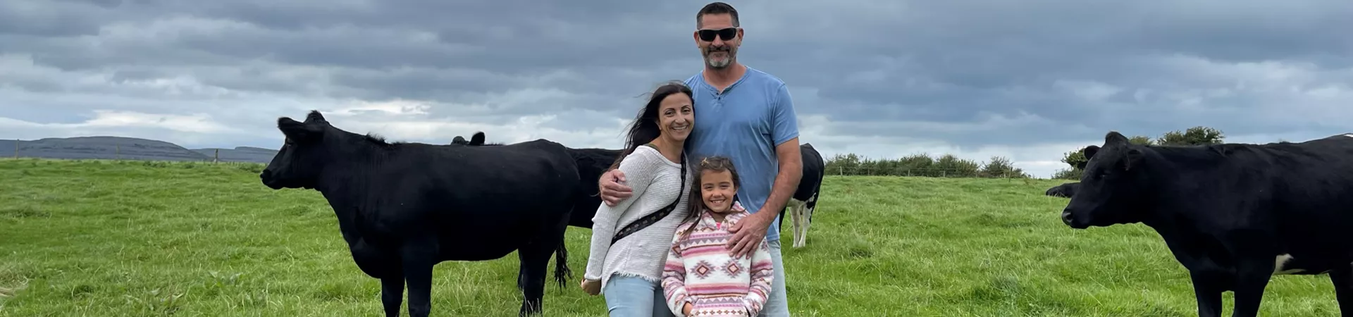 Family at the Kelly Burren Farm with two black cows in a green field